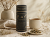 Lactation tea canister with a cup and tea leaves on a table.