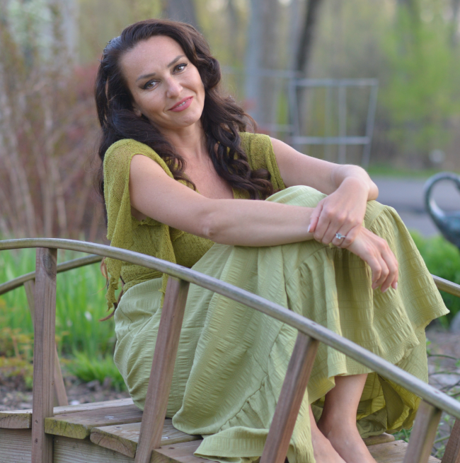 The Milky Wave founder Liliya sitting outdoors on a wooden bridge in a green dress